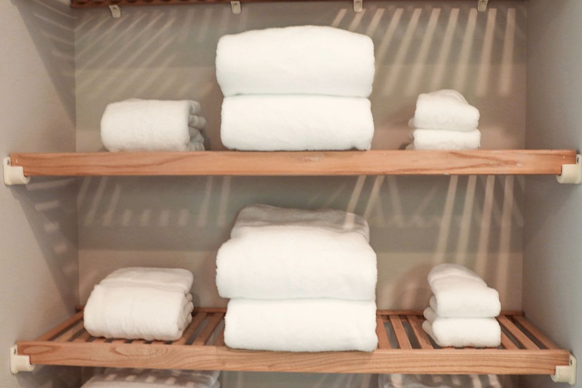 White folded towels neatly stacked on wooden shelves in a closet.