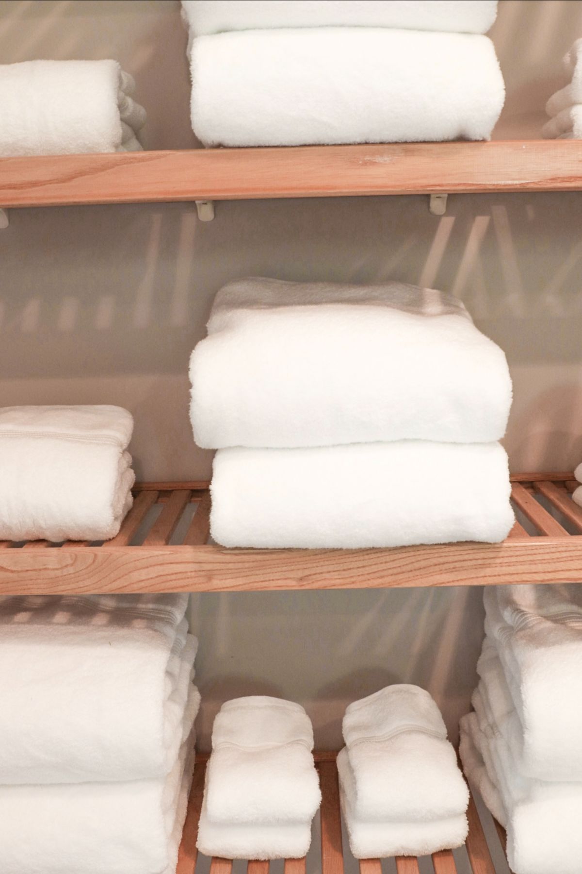 White folded towels stacked on wooden shelves in a closet.