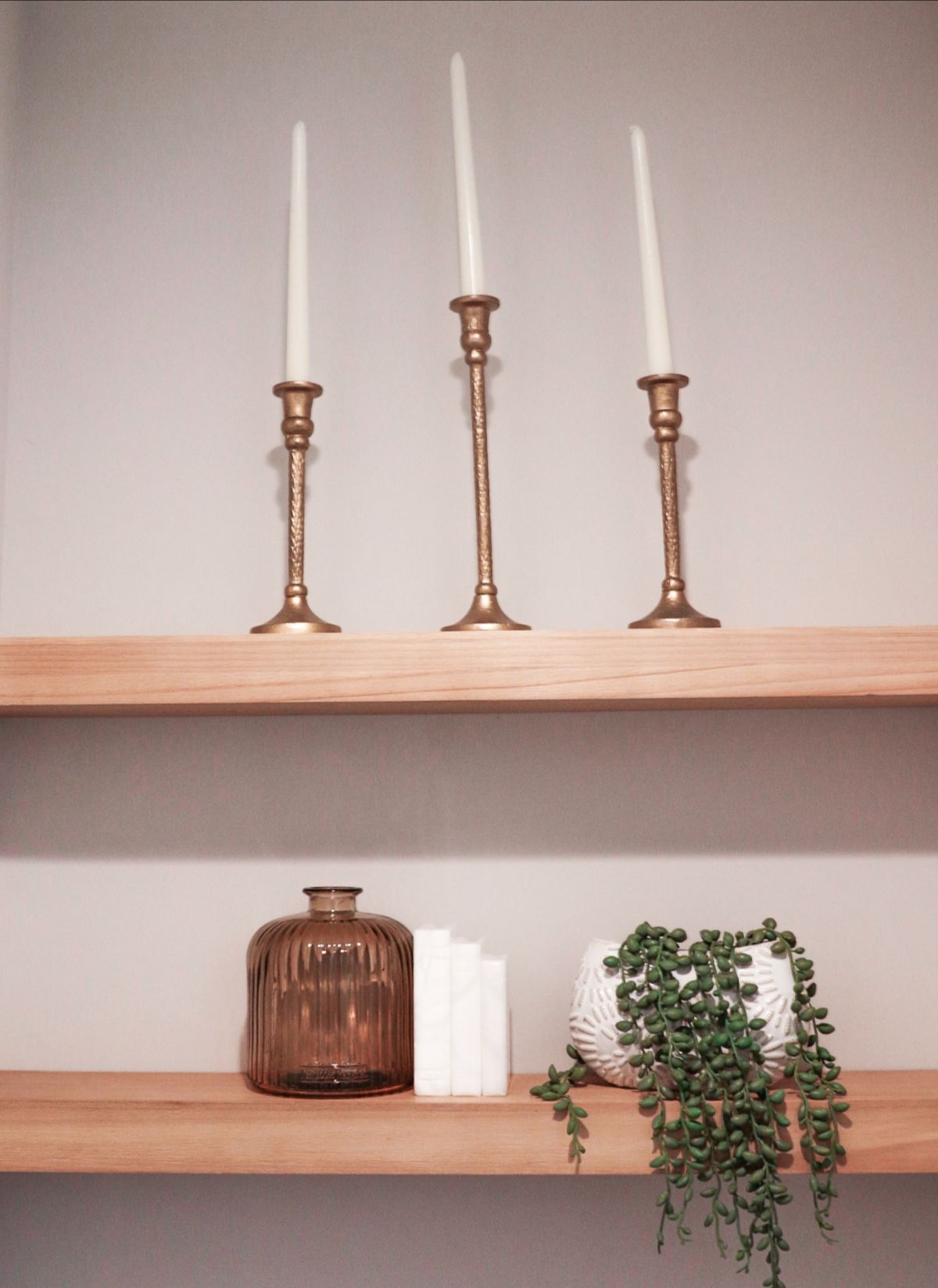 Two wooden shelves with brass candle holders, amber vase, white books, and trailing plant.