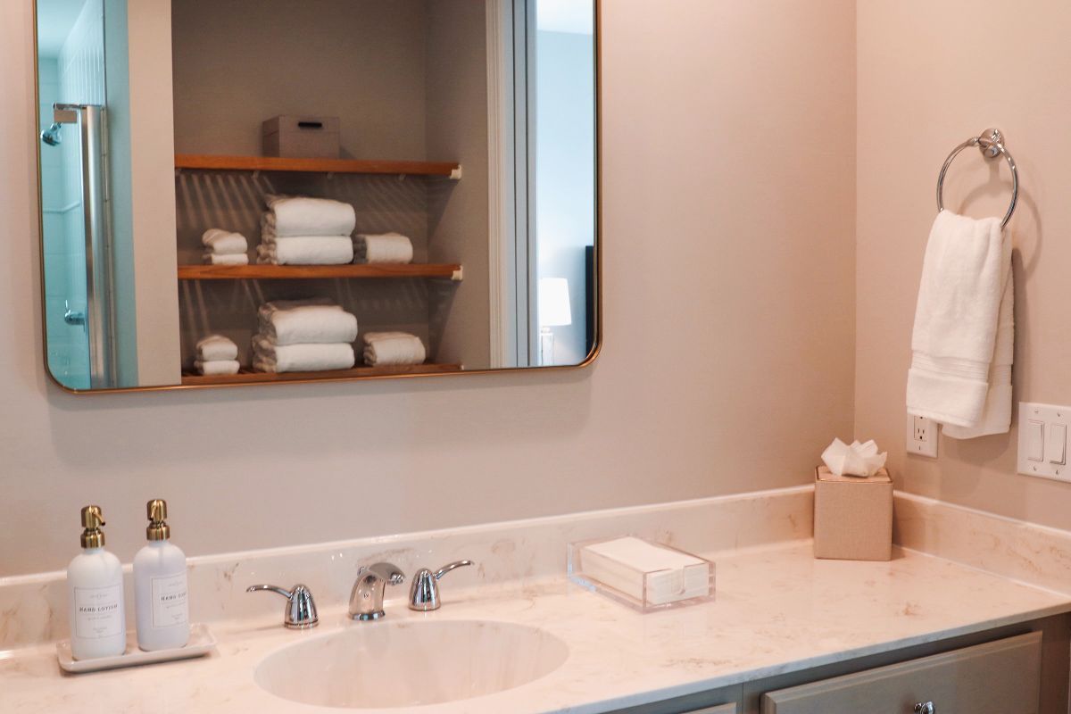 Bathroom with mirror, sink, and shelves holding towels. Pale pink walls.