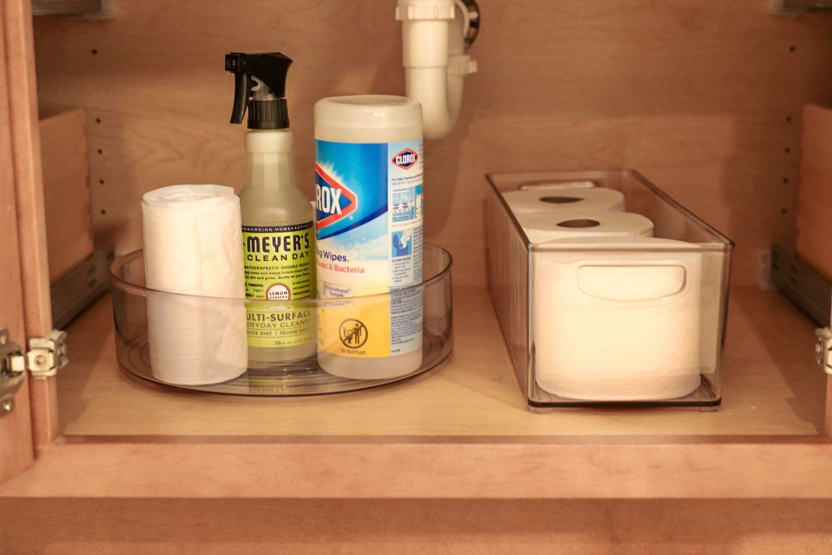 Bathroom cabinet with cleaning supplies and toilet paper.