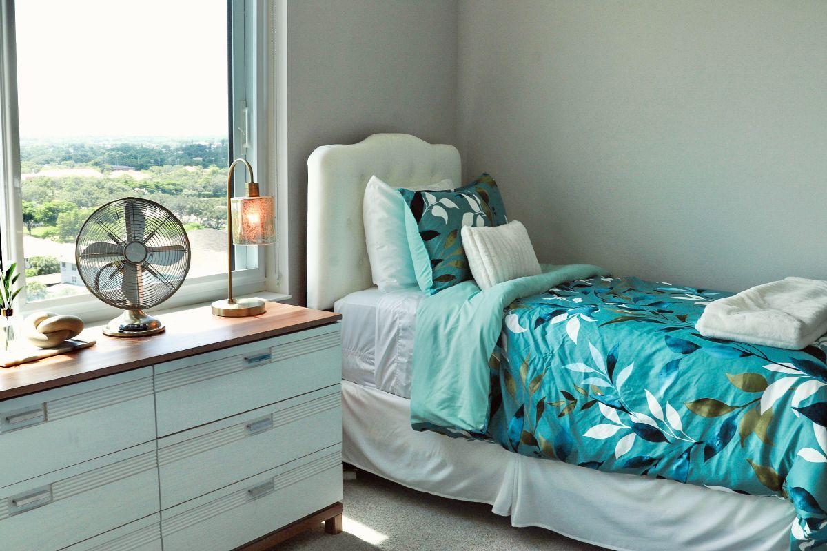 Bedroom with a bed, dresser, window, and decorative fan. The bedding is teal with a floral pattern.