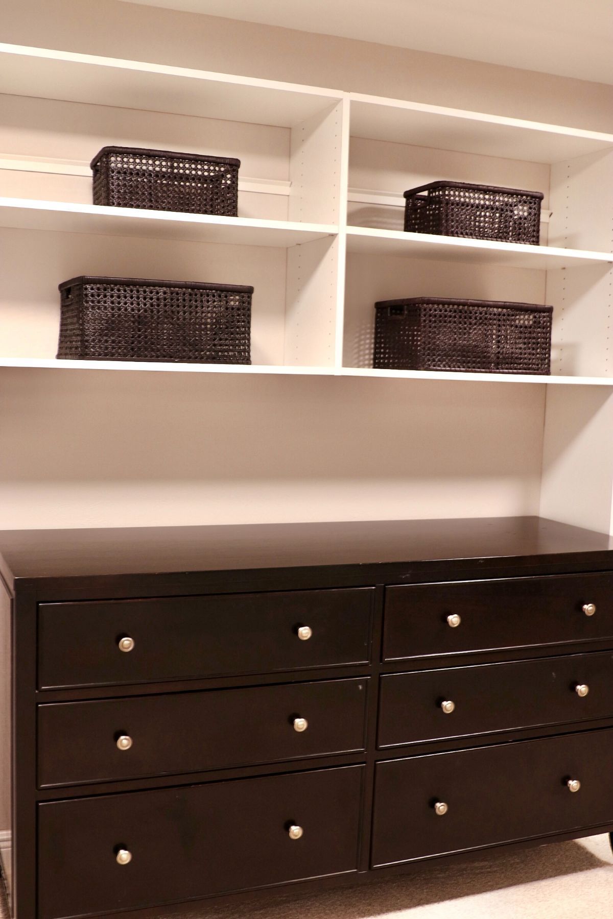 Dark dresser below white shelves with wicker storage baskets.