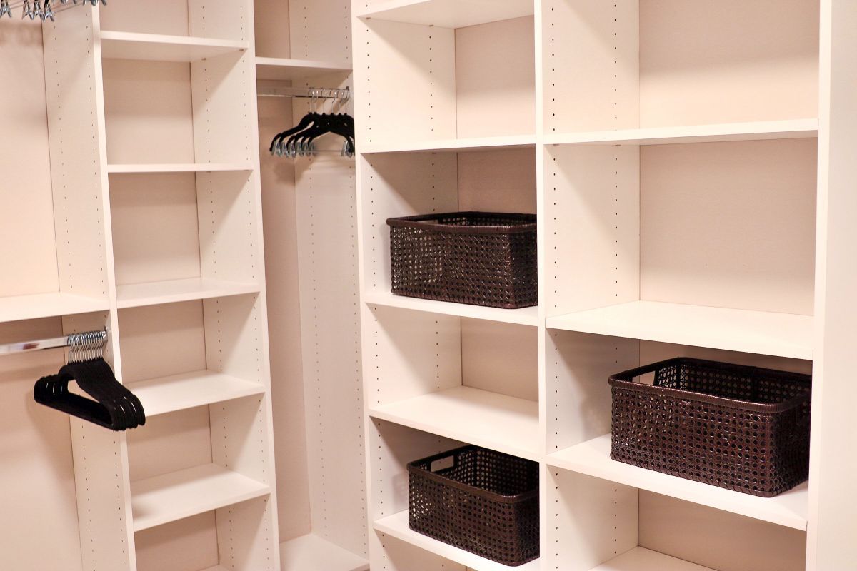 White organized closet shelving with clothes hangers and brown storage baskets.