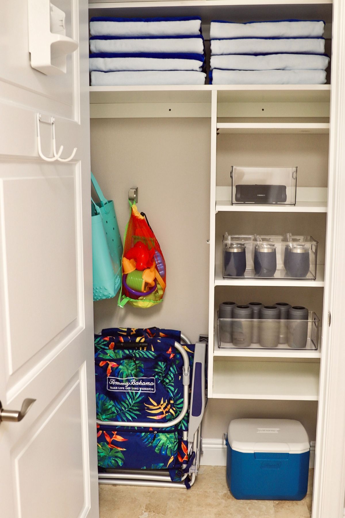 A neatly organized closet with towels, containers, bags, a chair, and a cooler.
