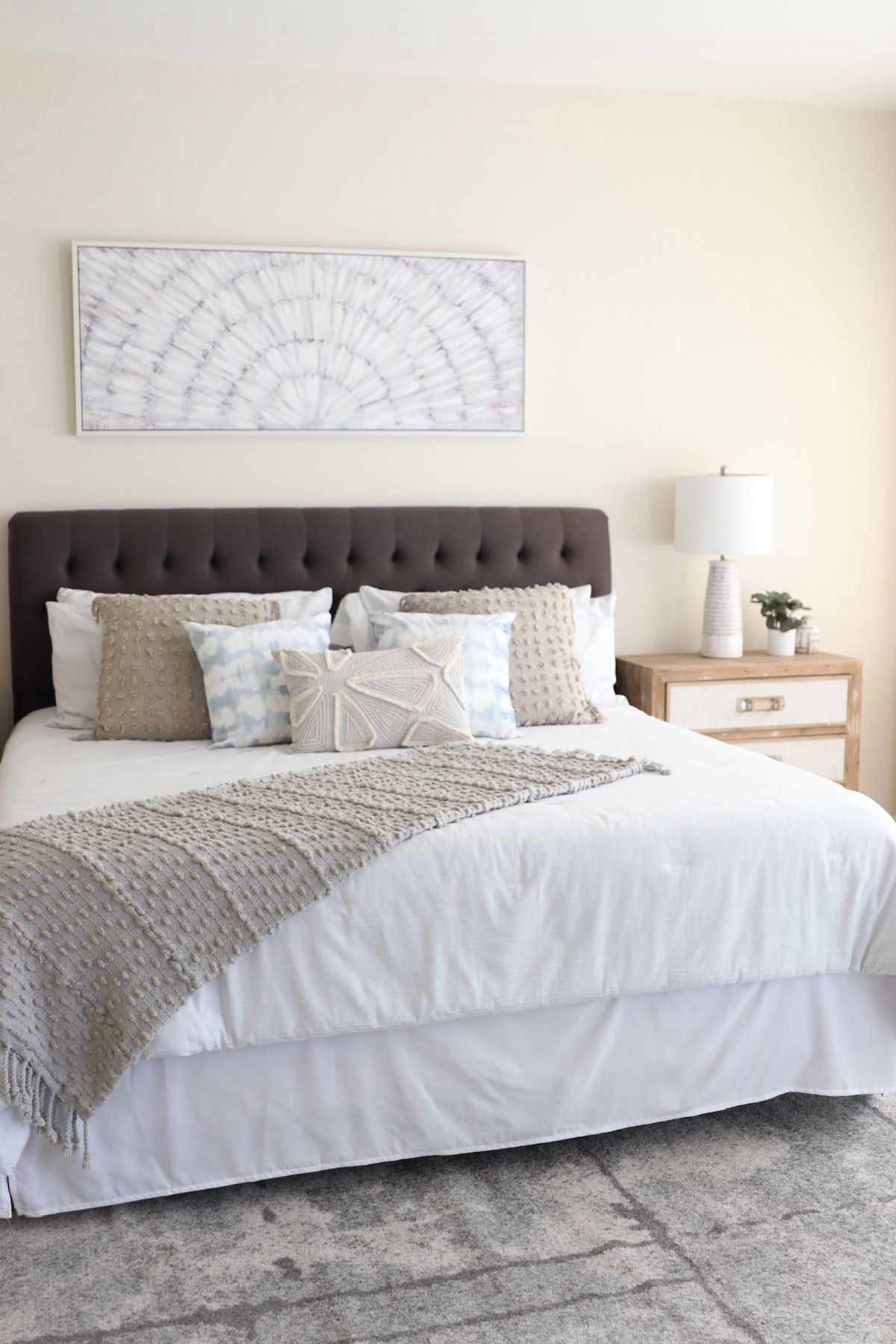 Bedroom with bed, neutral colors, tufted headboard, decorative pillows, and artwork.