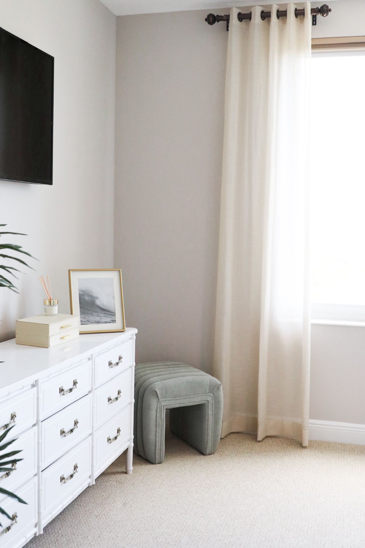 White dresser with decor, light green stool, and a window with cream curtains in a bedroom.