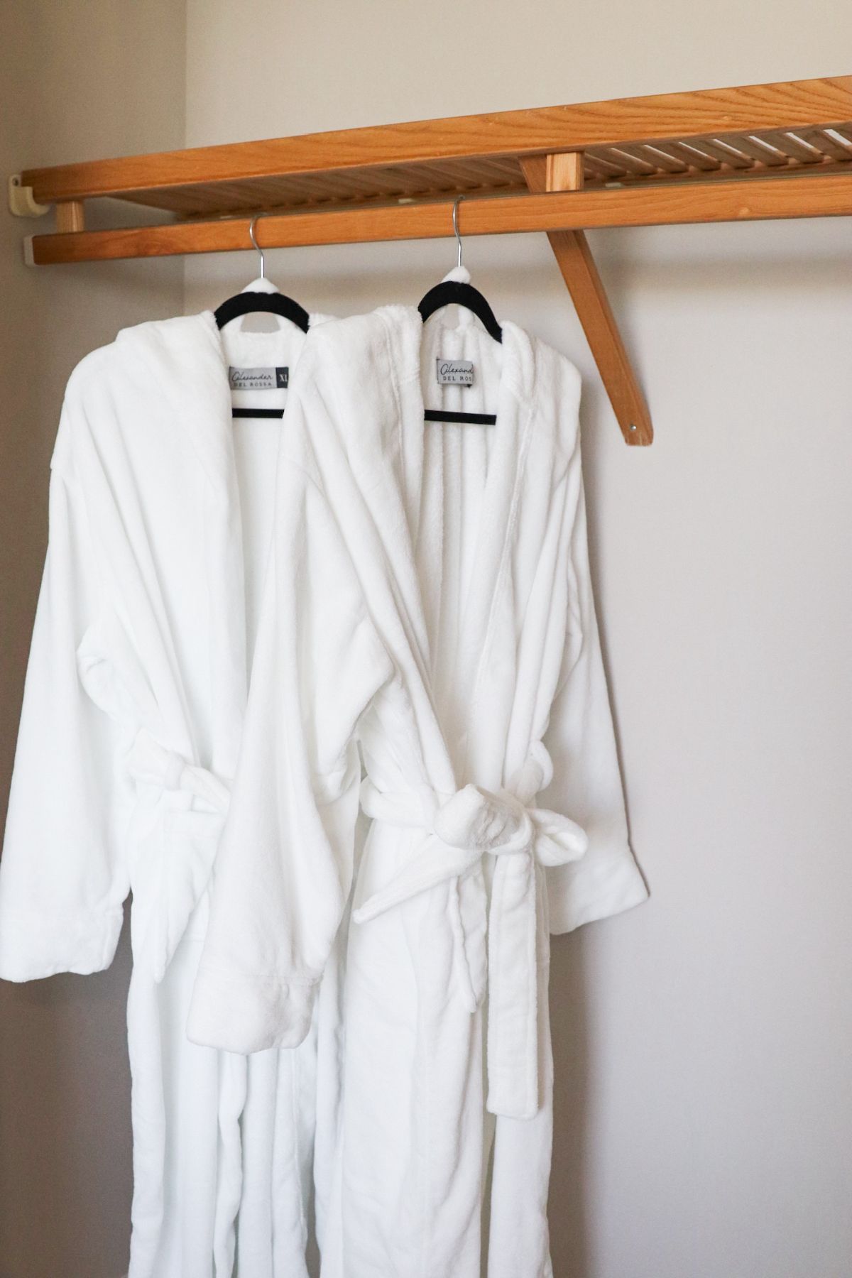 Two white bathrobes hanging in a closet on black hangers.
