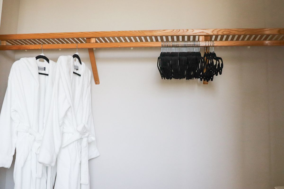 Closet with two white robes and several black umbrellas hanging from a wooden bar.