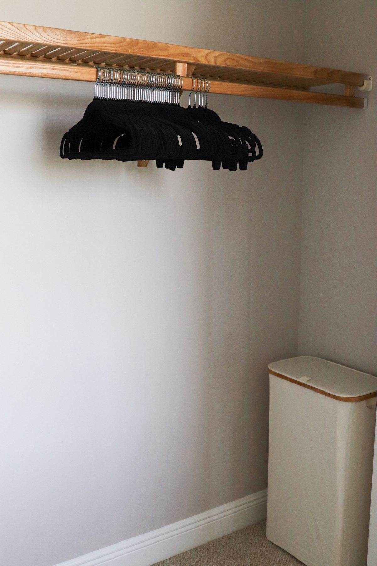 Closet with hangers on a wooden rod and a hamper in a neutral-colored room.