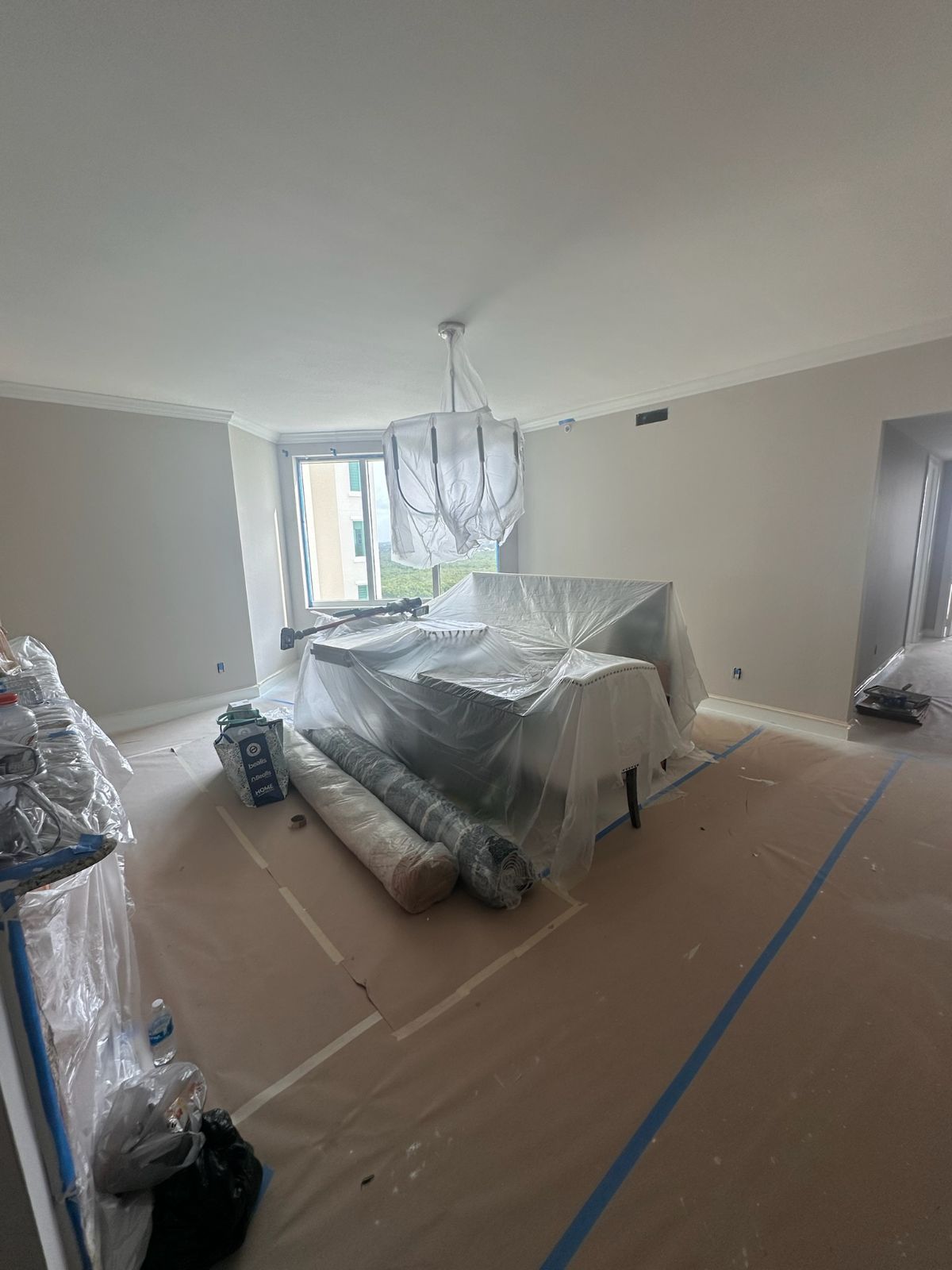 Room with protective coverings over furniture and flooring, undergoing renovations.