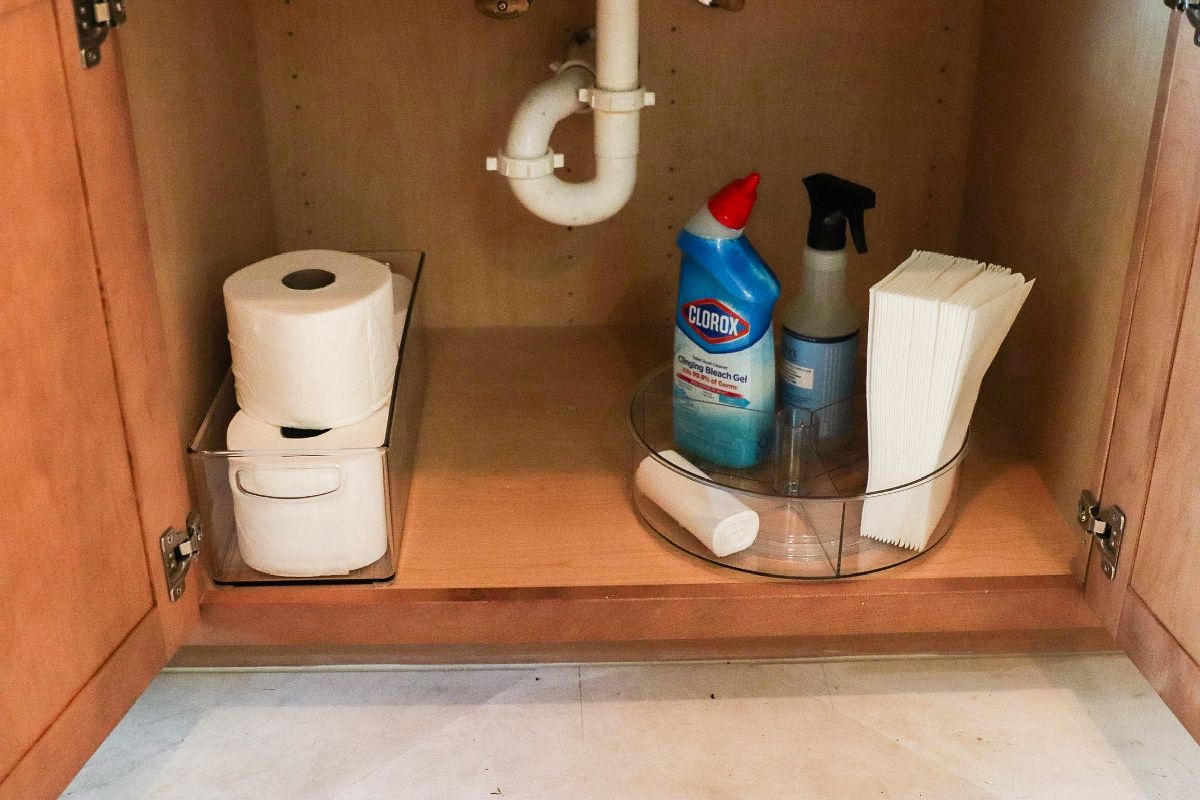 Bathroom cabinet with toilet paper, cleaning supplies, and paper towels.