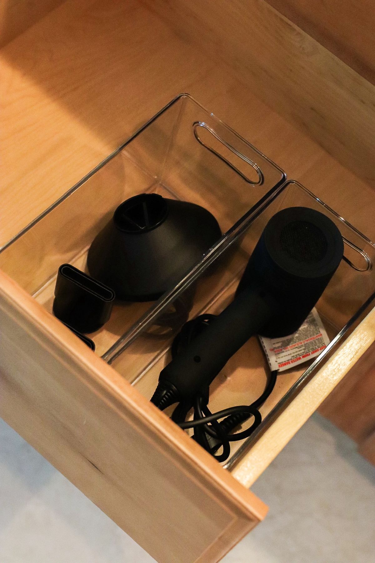 Hair dryer and attachments in a clear drawer organizer inside a wooden drawer.