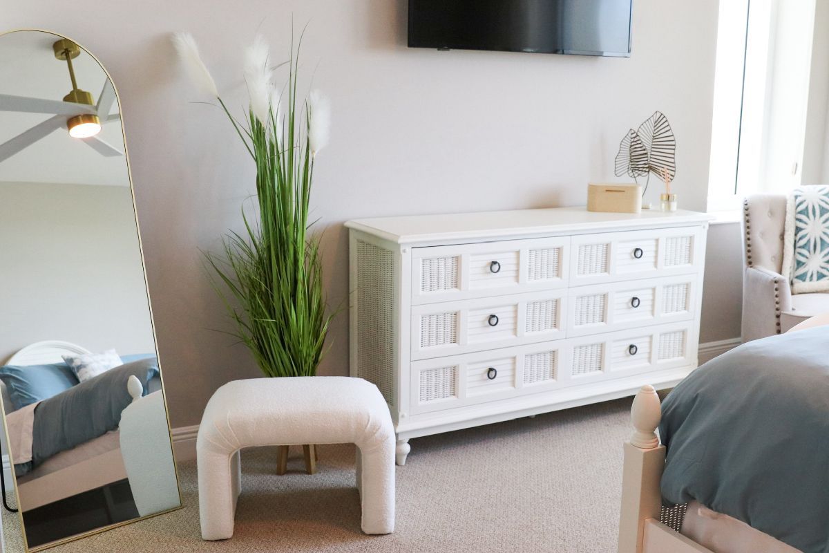 Bedroom with white dresser, arched mirror, tall plant, and blue bedding.