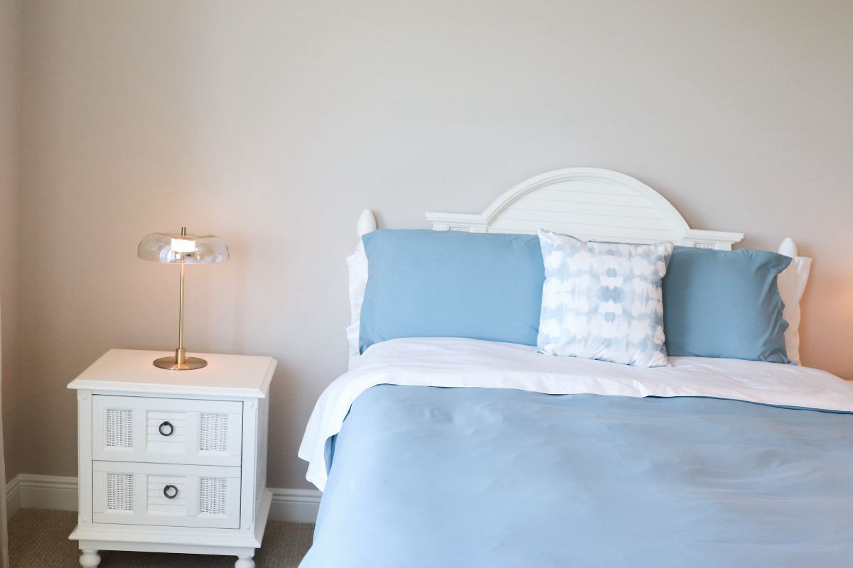 Bedroom with white furniture, light blue bedding, and a gold lamp on a nightstand.