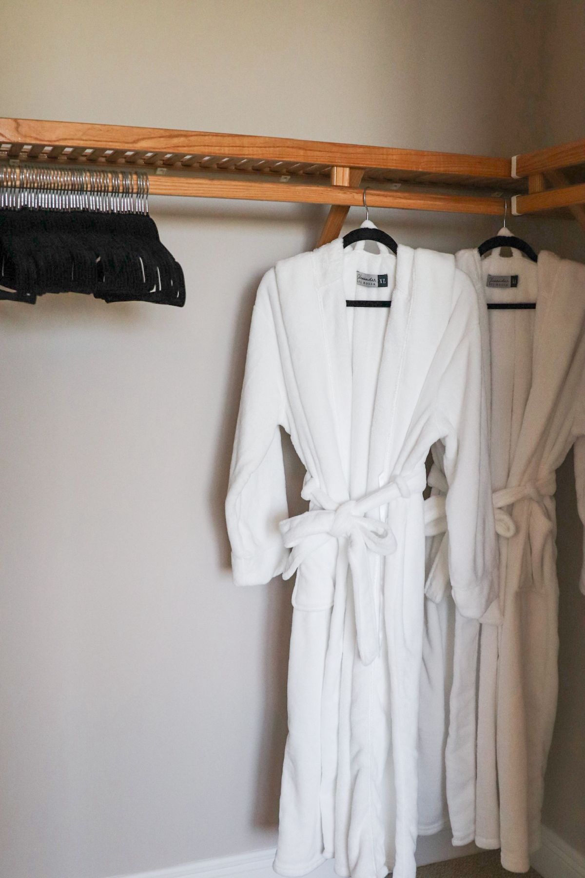 White bathrobes hanging in a closet, next to a rack of black hangers.