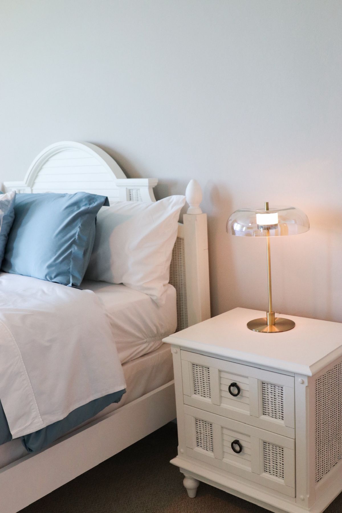 White bedroom with a bed, blue pillows, and a nightstand with a lamp.