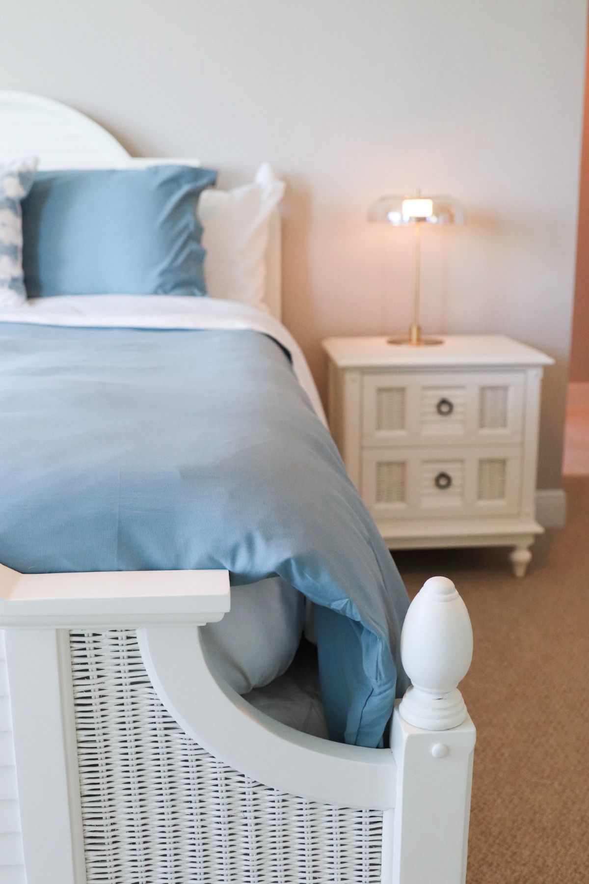 White bed with blue bedding and nightstand with lamp.