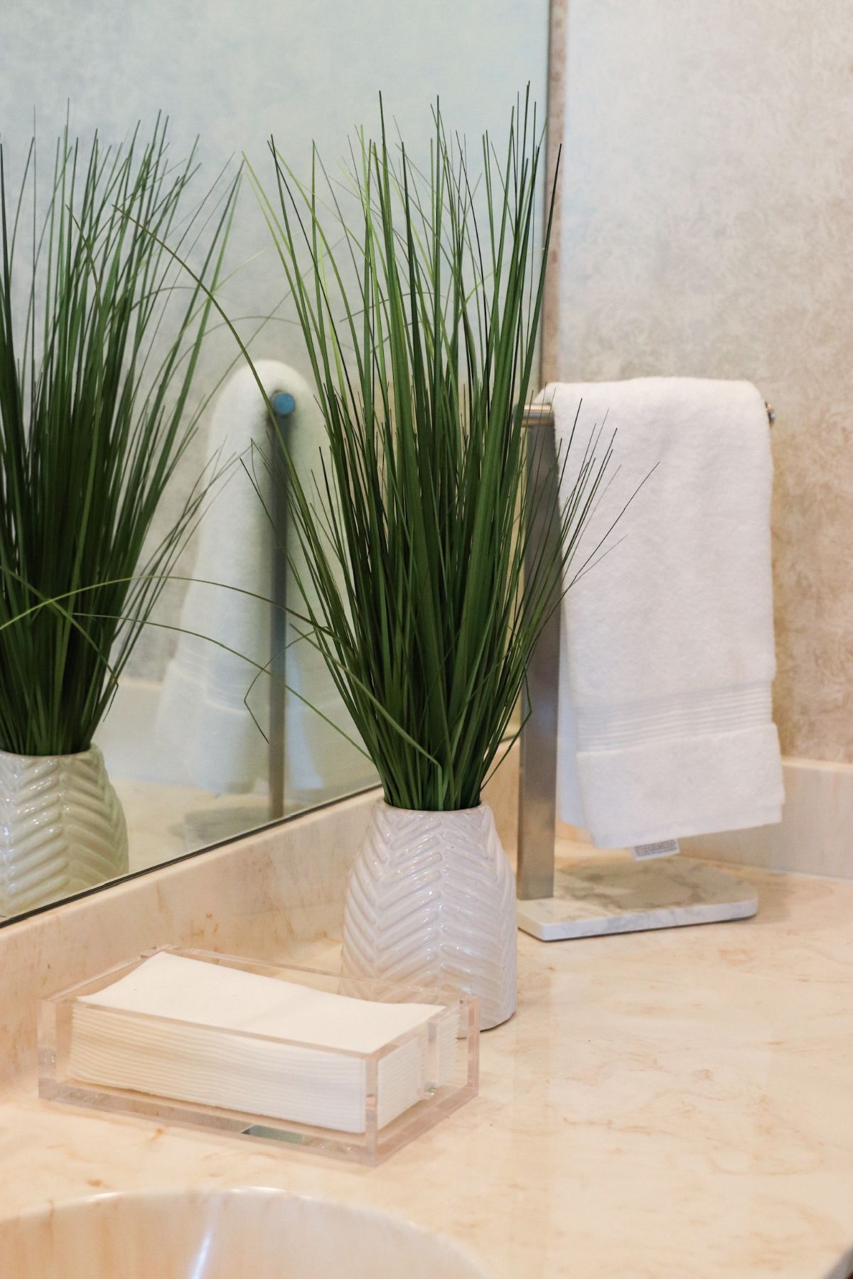 Bathroom counter with a white towel, tall green grass in a vase, and a soap dish.