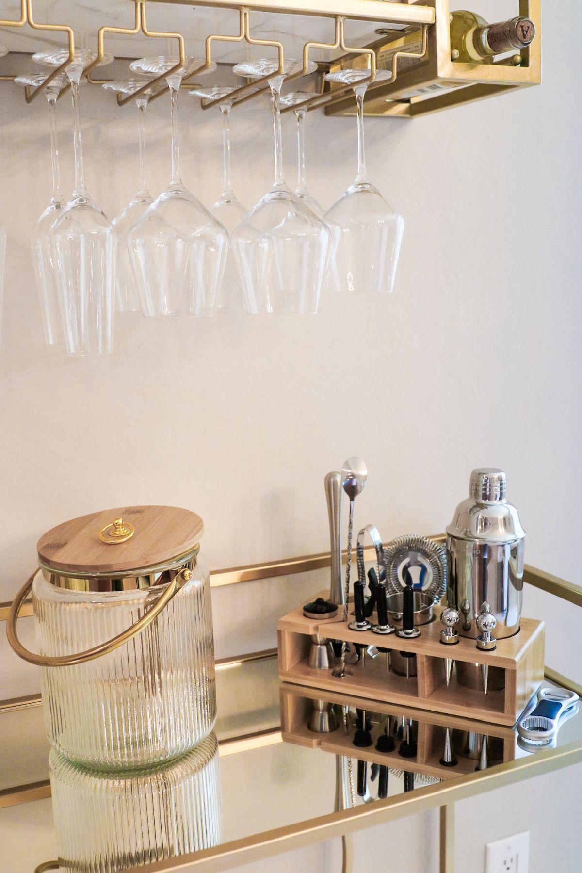 Wine bar with hanging glasses, ice bucket, and bar tools on mirrored surface.