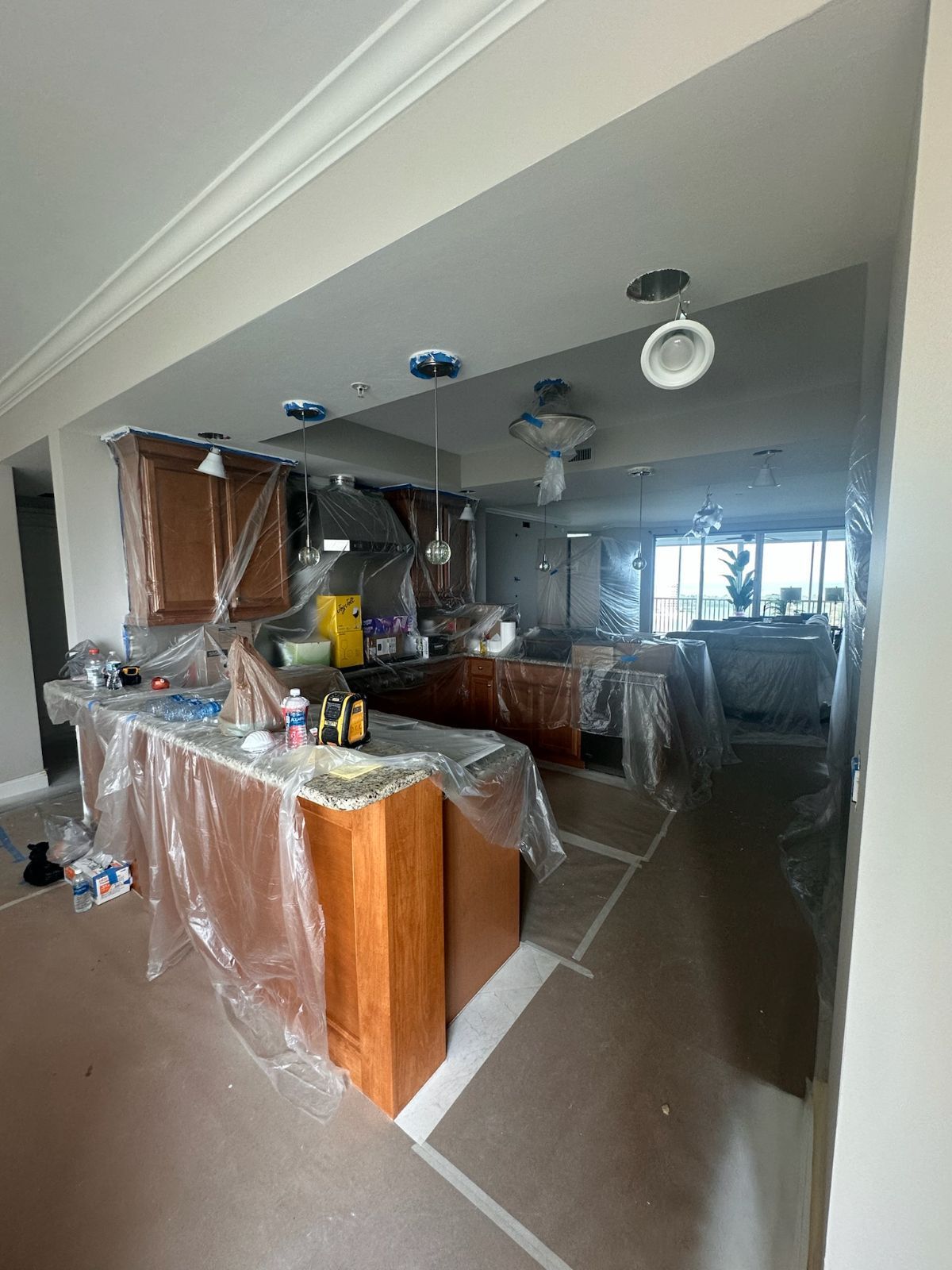 Kitchen under renovation, cabinets and counters covered in plastic, ceiling with exposed light fixtures.