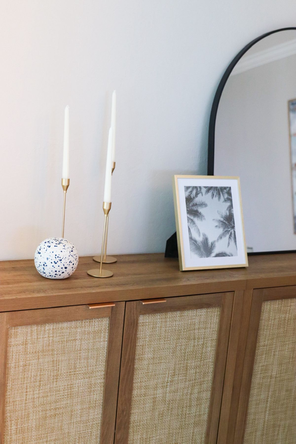 Wooden cabinet with candles, framed art, and mirror against a white wall.