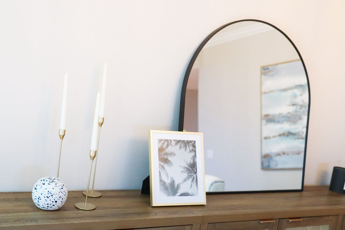 Wooden console table with candles, a framed photo, and a large black-framed mirror.