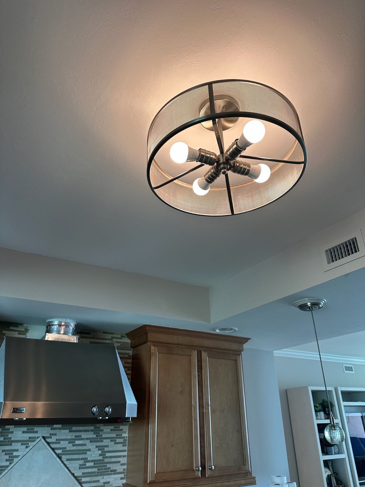 Ceiling light fixture with five bulbs, over a kitchen with cabinets, and a vent hood.