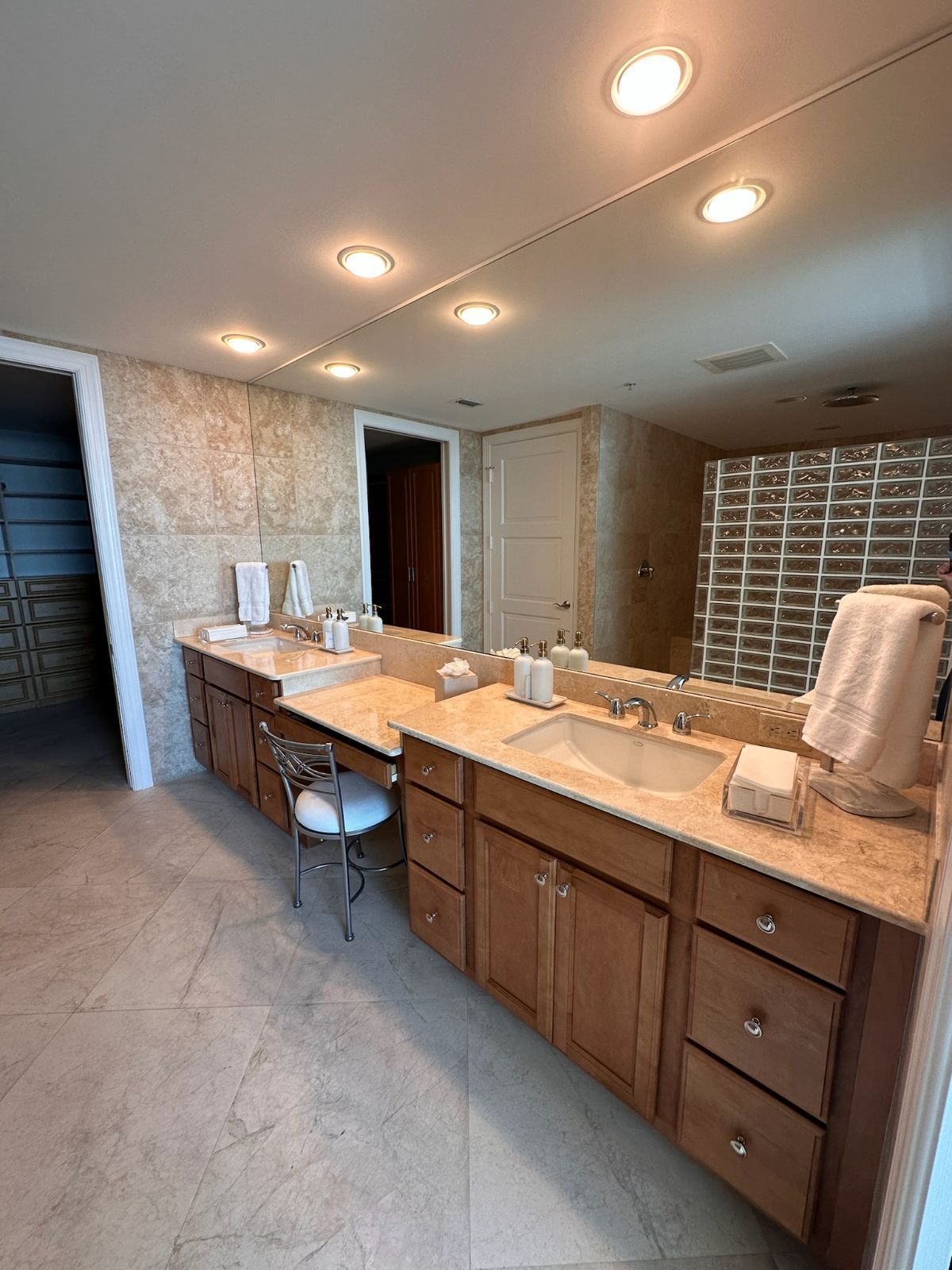 Spacious bathroom with dual sinks, large mirror, wooden cabinets, and beige tile.