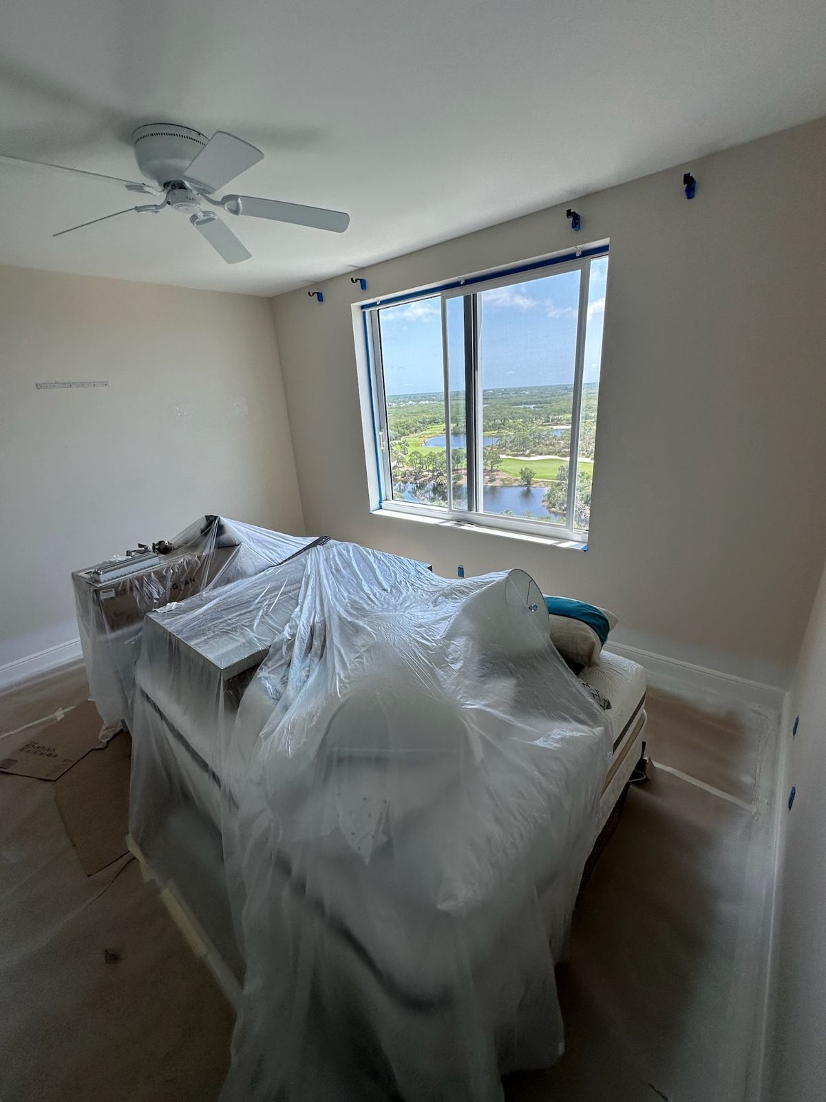 Bedroom with bed and furniture covered in plastic for protection, window with a view.