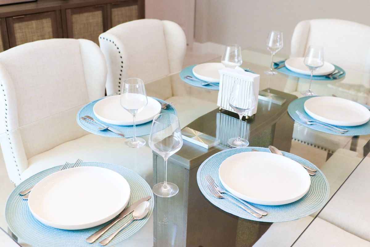 Dining table set with six places, white plates, blue placemats, and tall wine glasses.