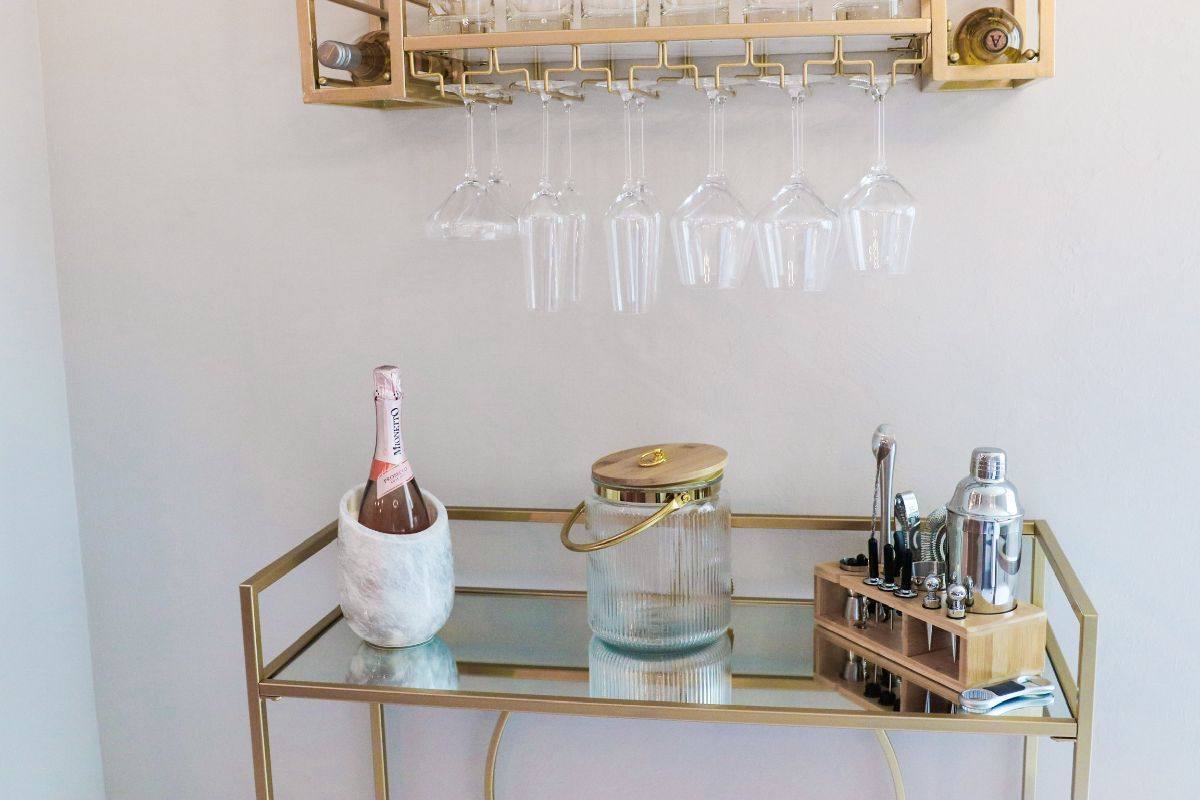 Gold bar cart with a wine rack holding glasses and a champagne bottle.