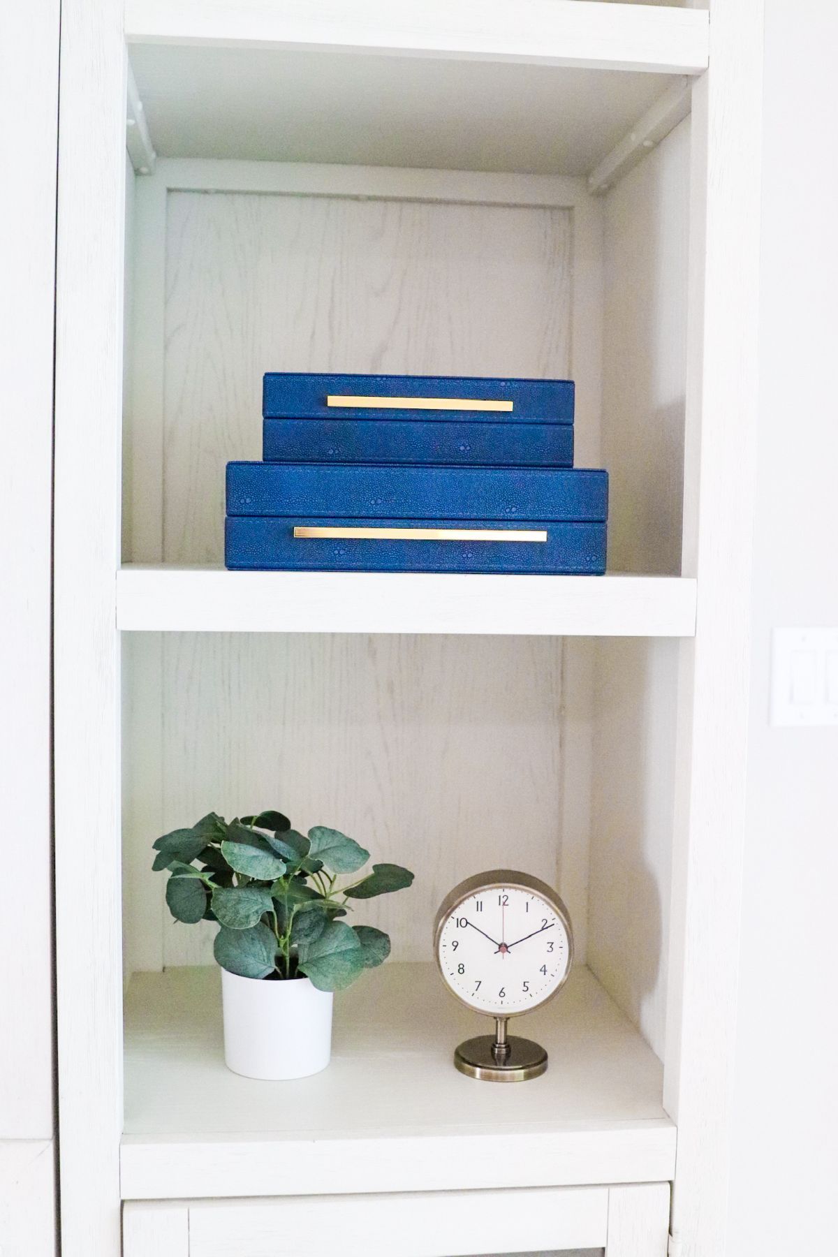 White bookshelf with blue boxes, a potted plant, and a clock.