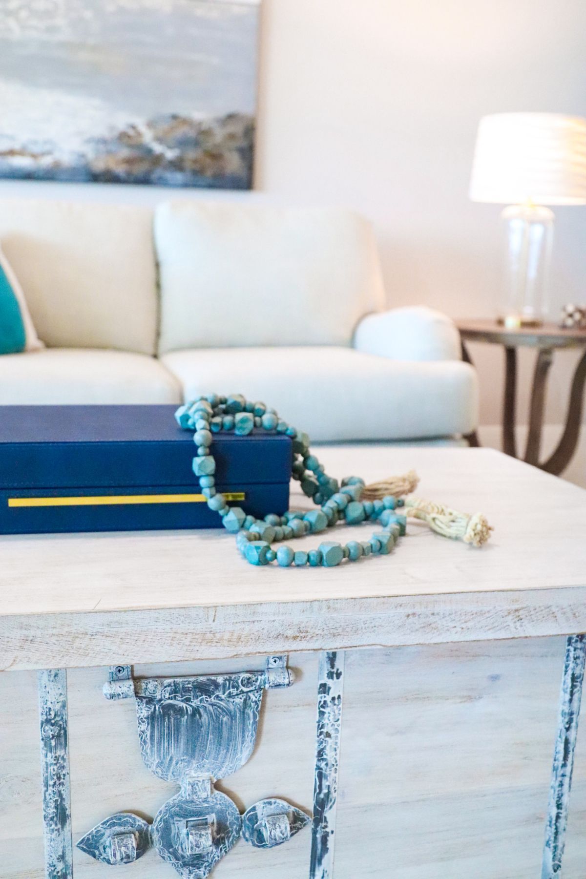 White coffee table with blue box and beaded necklace in front of a white couch.