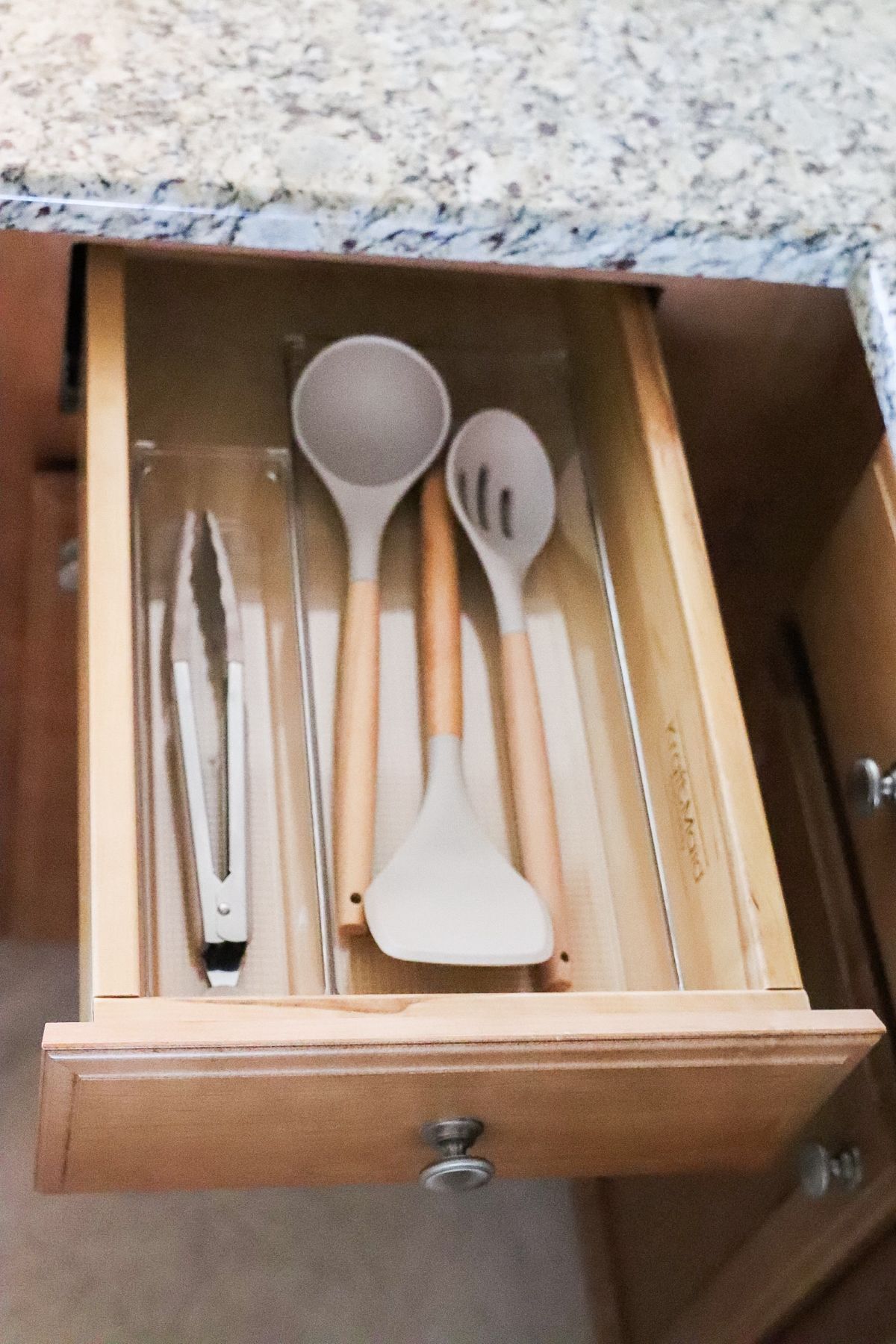 Kitchen drawer with utensils: tongs, spoon, spatula, slotted spoon, and organizer.