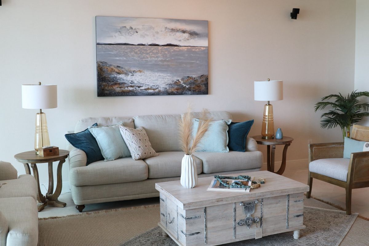 Living room with light-colored sofa, teal pillows, and a seascape painting above it.