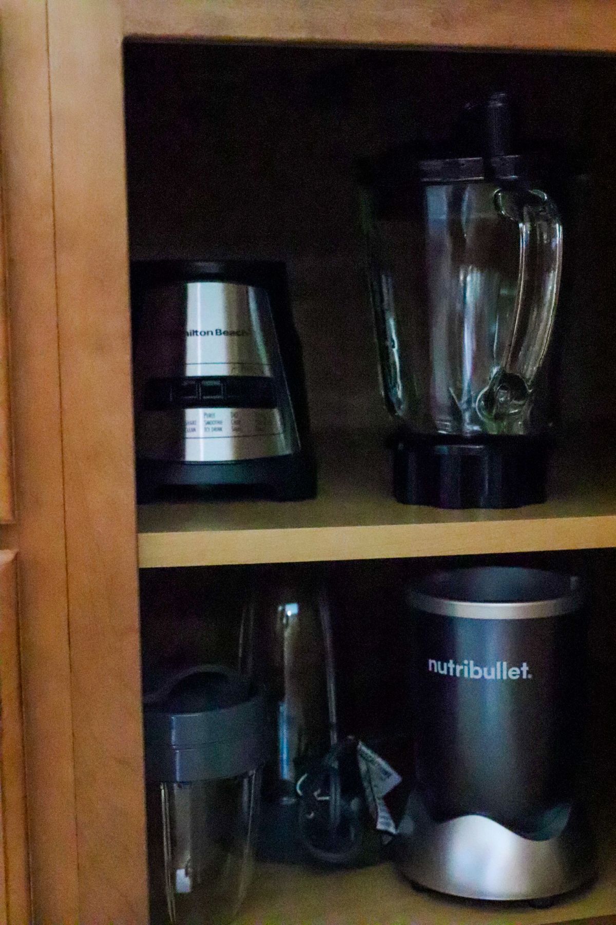 Blenders and Nutribullet stored inside a wooden kitchen cabinet.