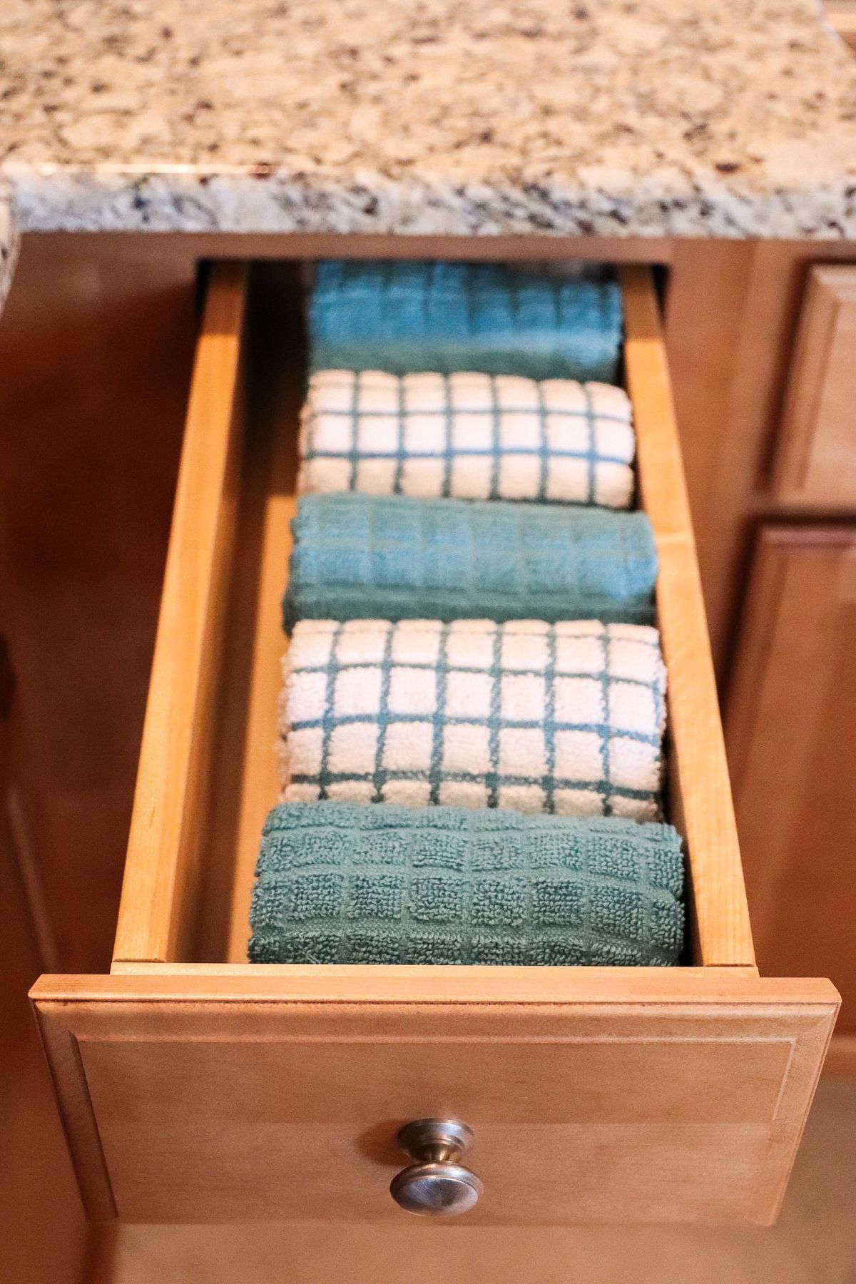 Drawer with neatly stacked teal and white checkered kitchen towels.
