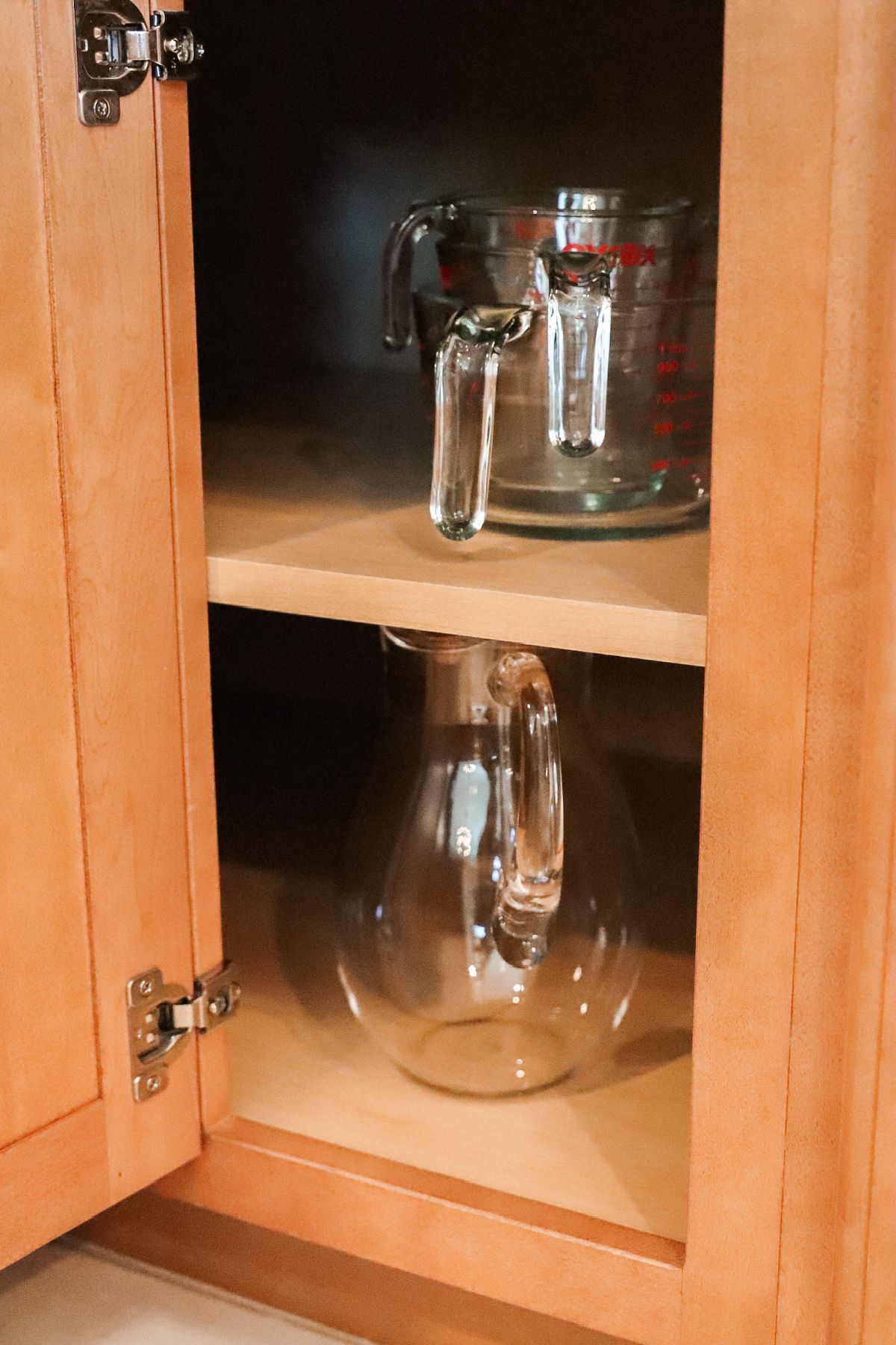 Cabinet open, showing two glass measuring cups and a pitcher on shelves.