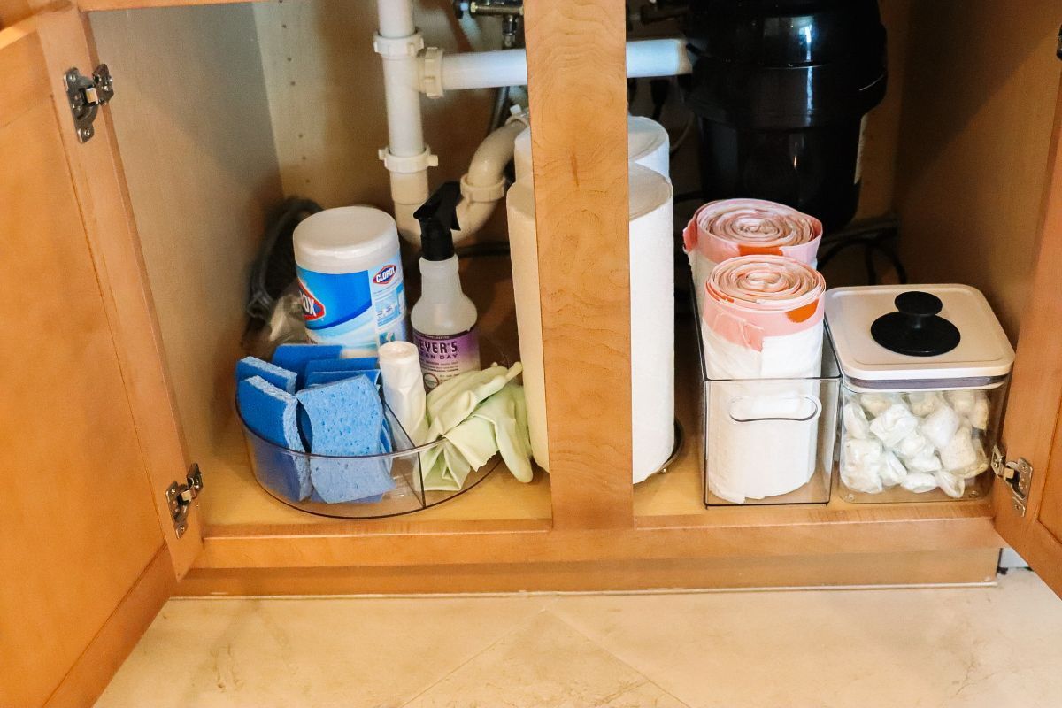 Under-sink cabinet organization: cleaning supplies, sponges, paper towels, and containers.