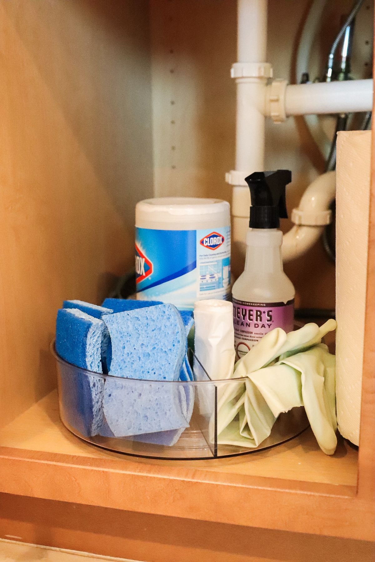 Cleaning supplies organized on a clear, divided lazy Susan inside a cabinet.