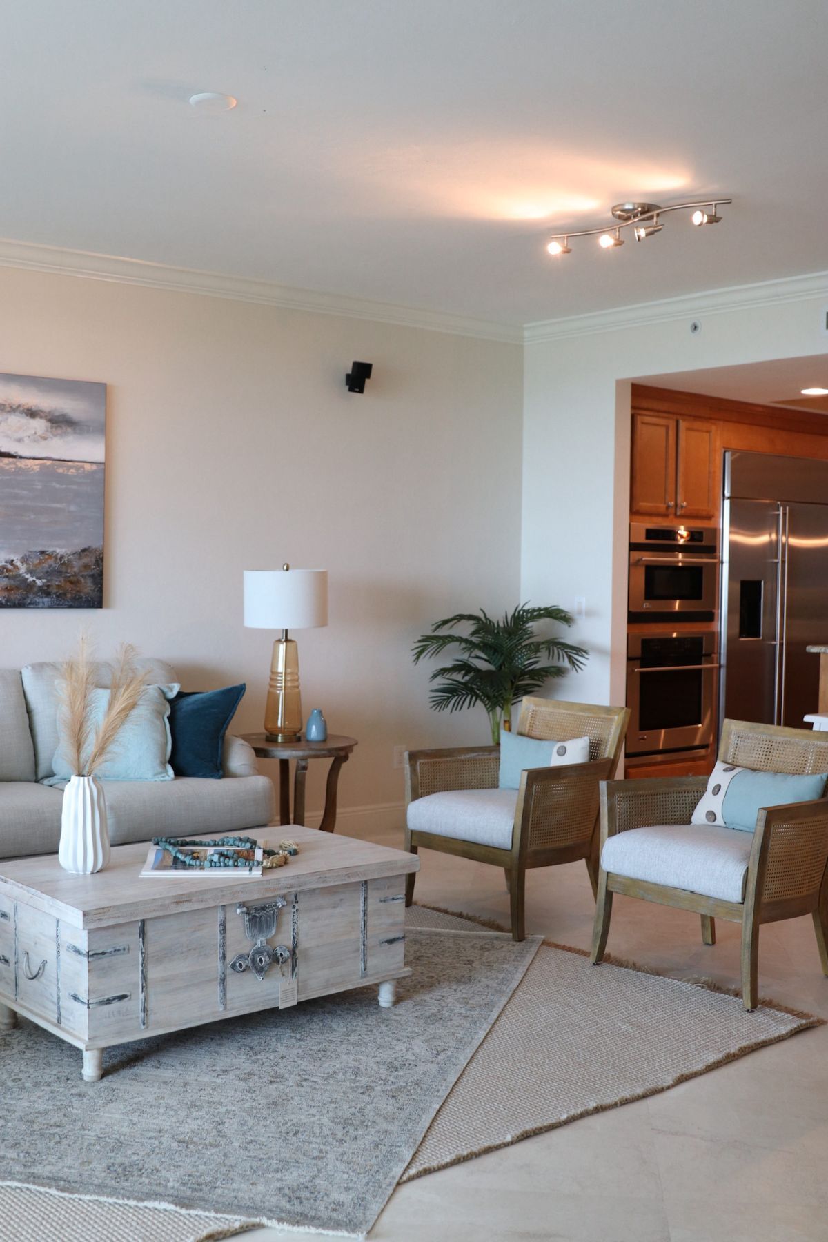Living room with beige walls, light furniture, and kitchen in background.