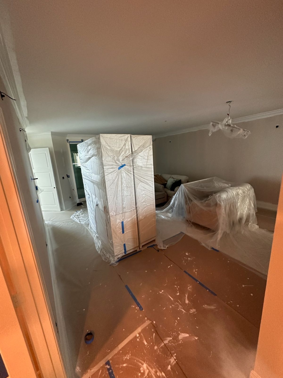 Room under construction, with a large wrapped item, furniture covered, and plastic on the floor.