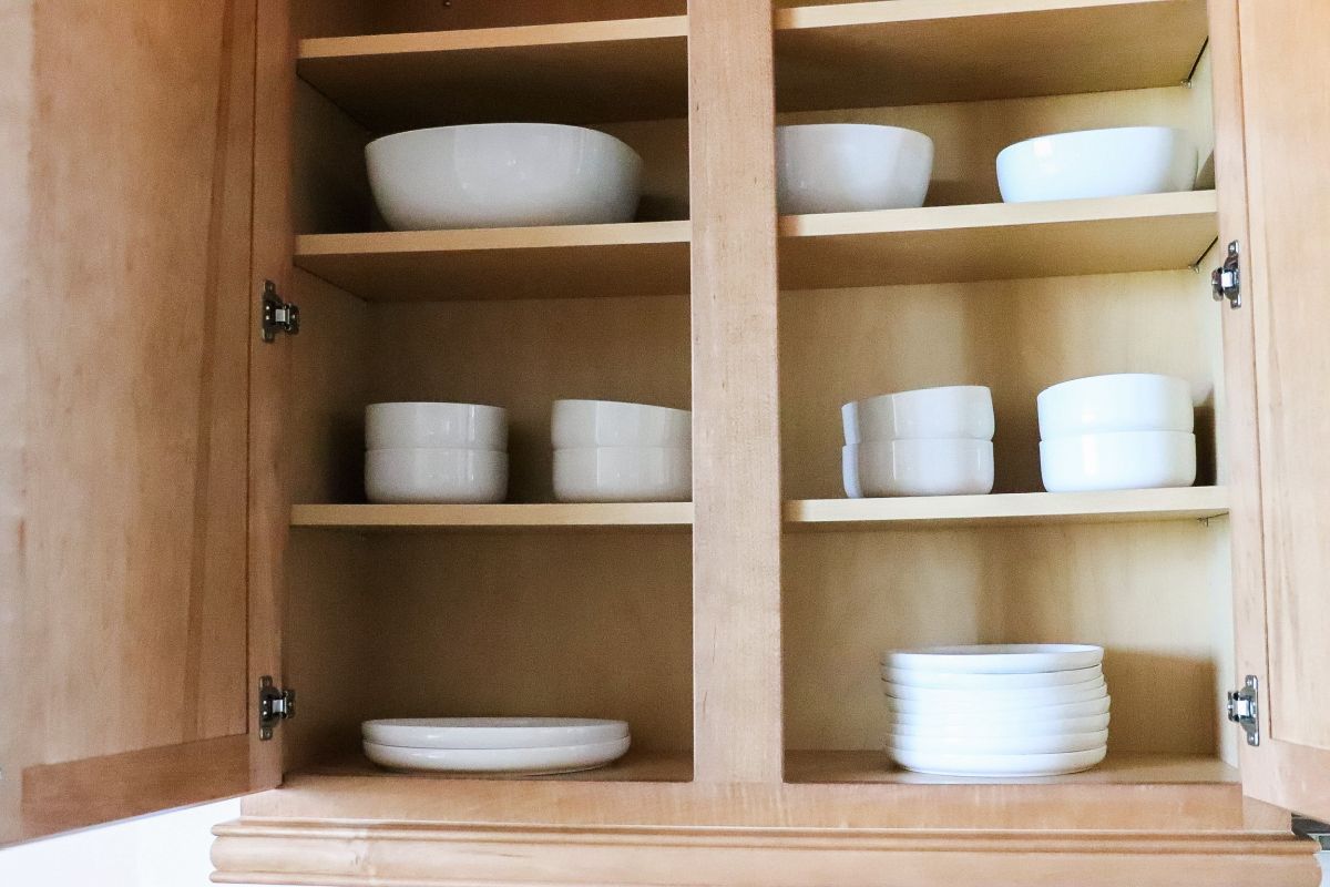 Wooden kitchen cabinet with white dishes stacked on shelves.