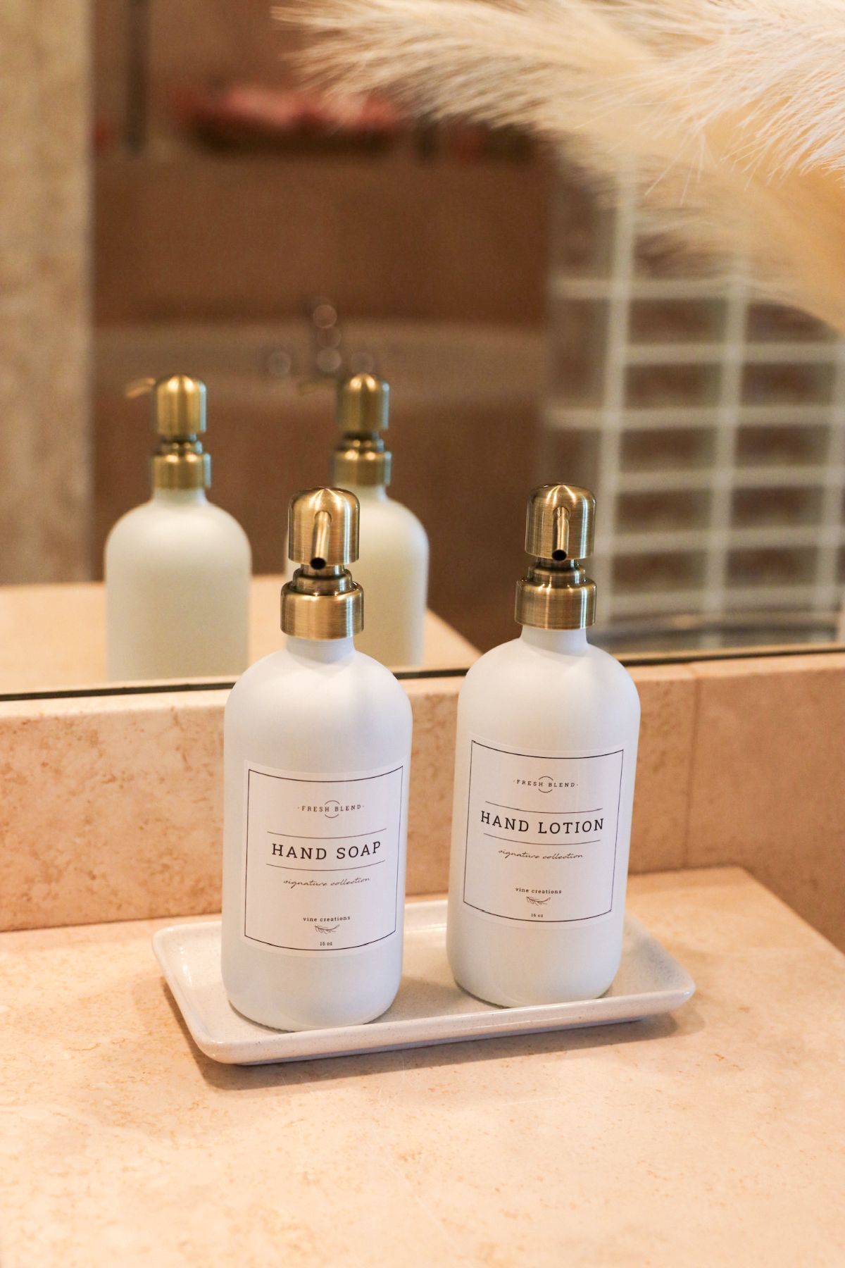 White bottles with gold pumps, labels, on a tray, in front of a mirror.