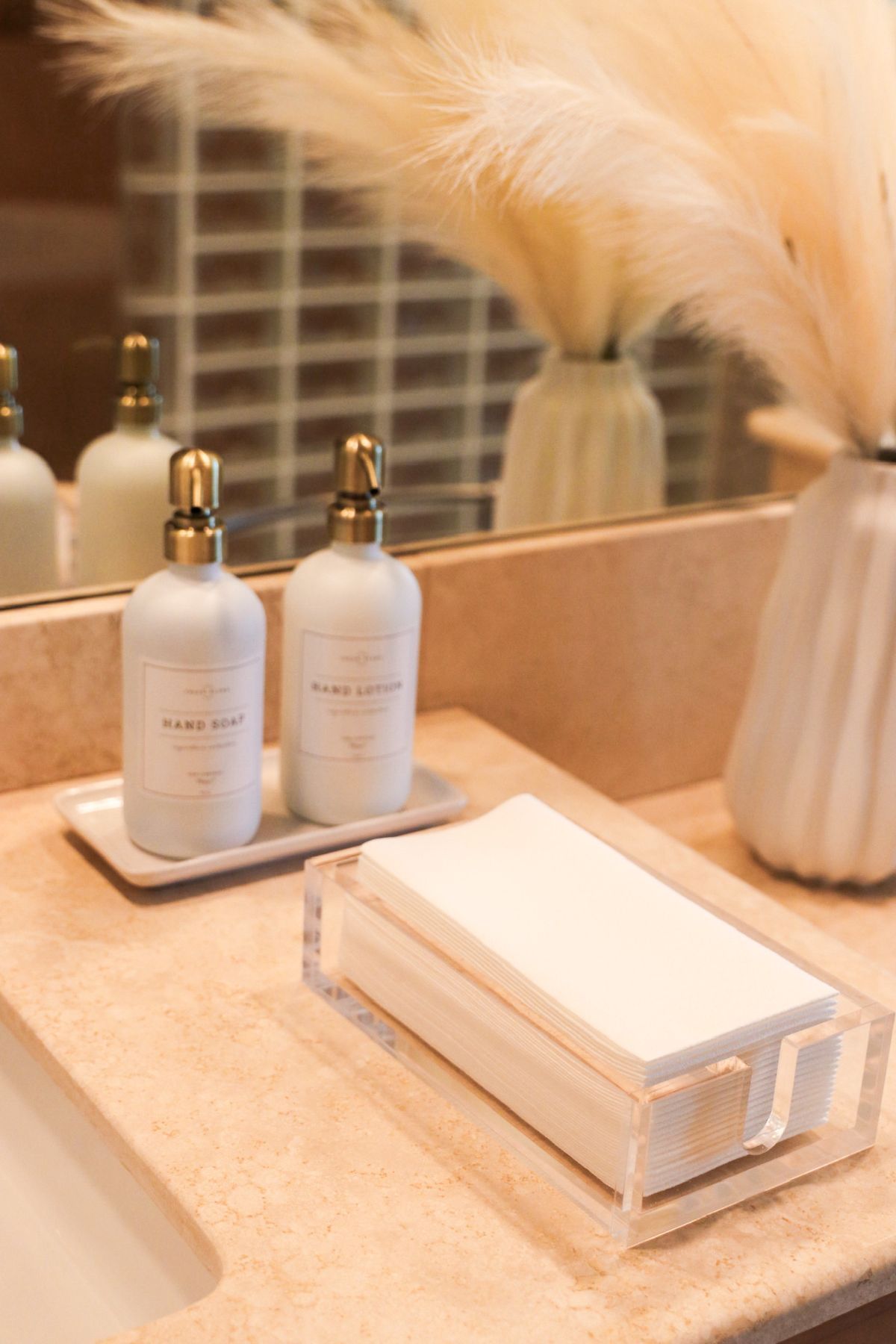 Bathroom countertop with soap dispensers, cotton pads, and pampas grass in vases.