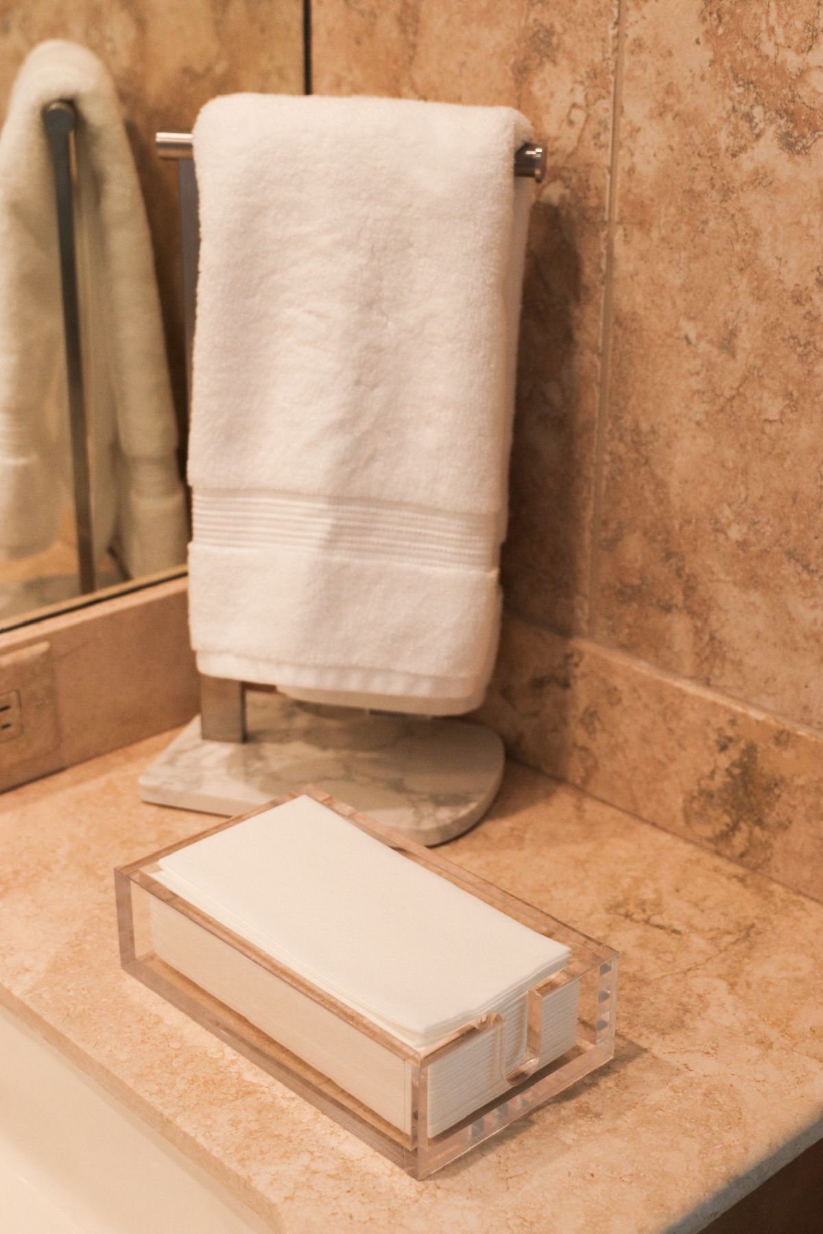 White hand towel on stand, tissue box on a beige counter in a bathroom with mirror.