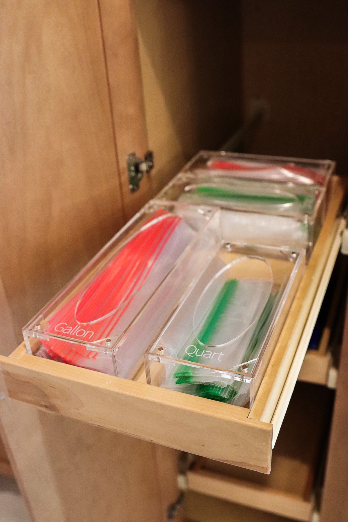 A pull-out cabinet drawer filled with clear acrylic containers holding colorful utensils.