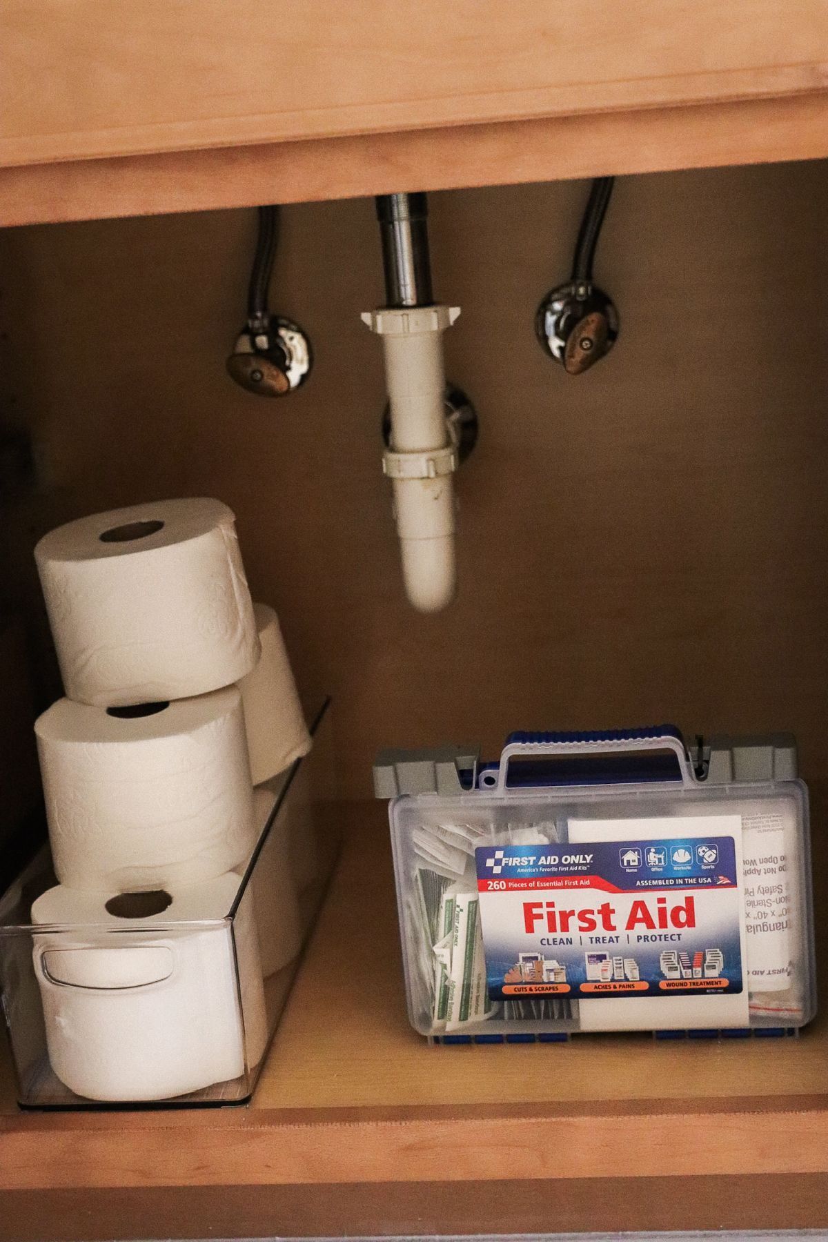 Bathroom cabinet with toilet paper rolls and a first aid kit.