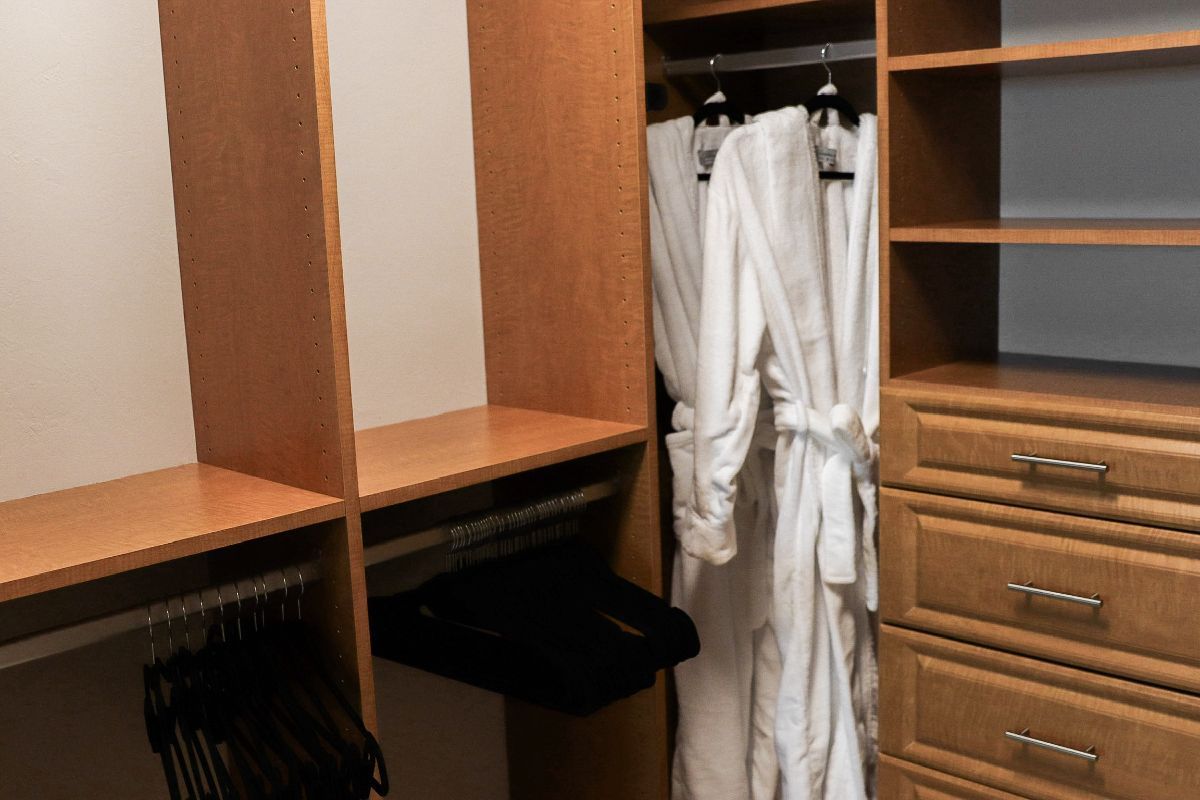 Walk-in closet with light wood shelving, clothes hanging, and drawers.